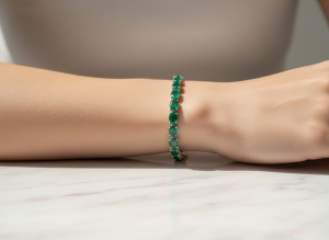 Woman's wrist resting on marble wearing a natural Colombian emerald tennis bracelet in white gold